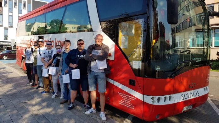 Grupa krwiodawców stojąca przed biało-czerwonym autobusem PCK