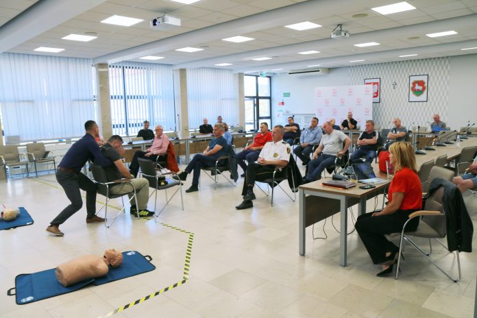 Strażnicy miejscy – wszechstronne szkolenia Szkolenia Strażników Miejskich. Na zdjęciu osoby biorące udział w szkoleniu na sali konferencyjnej, które oglądają praktyczny pokaz wyciągania rannej osoby z samochodu.