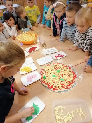 Zdjęcie. Kulinarne Podróże po Świecie w Nefrytowym Zakątku. Na zdjęciu dzieci wykonujące pracę plastyczną, wykonują papierową pizzę oraz makaron.