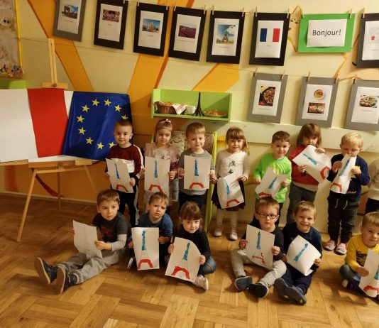 Zdjęcie. Kulinarne Podróże po Świecie w Nefrytowym Zakątku. Na zdjęciu grupa dzieci prezentująca swoje prace plastyczne- namalowane wieże Eiffla.