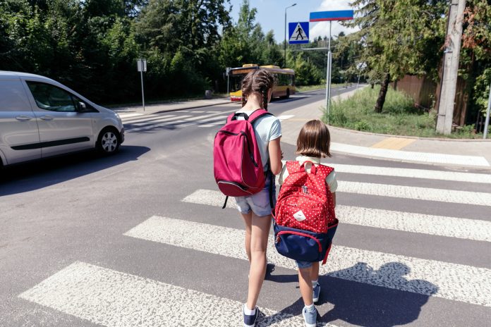 Bezpieczna droga do szkoły. Na zdjęciu dzieci z plecakami idące do szkoły po pasach dla pieszych.
