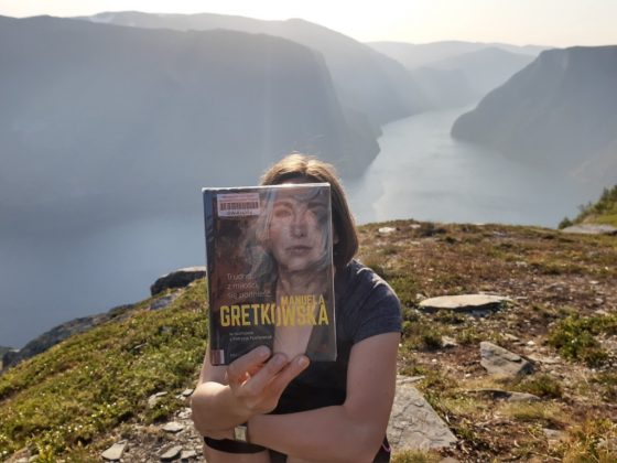 Kobieta na tle górskiego pejzażu, Jej twarz zasłania czytana książka. Włosy kobiety dopełniają portretu osoby na okładce.