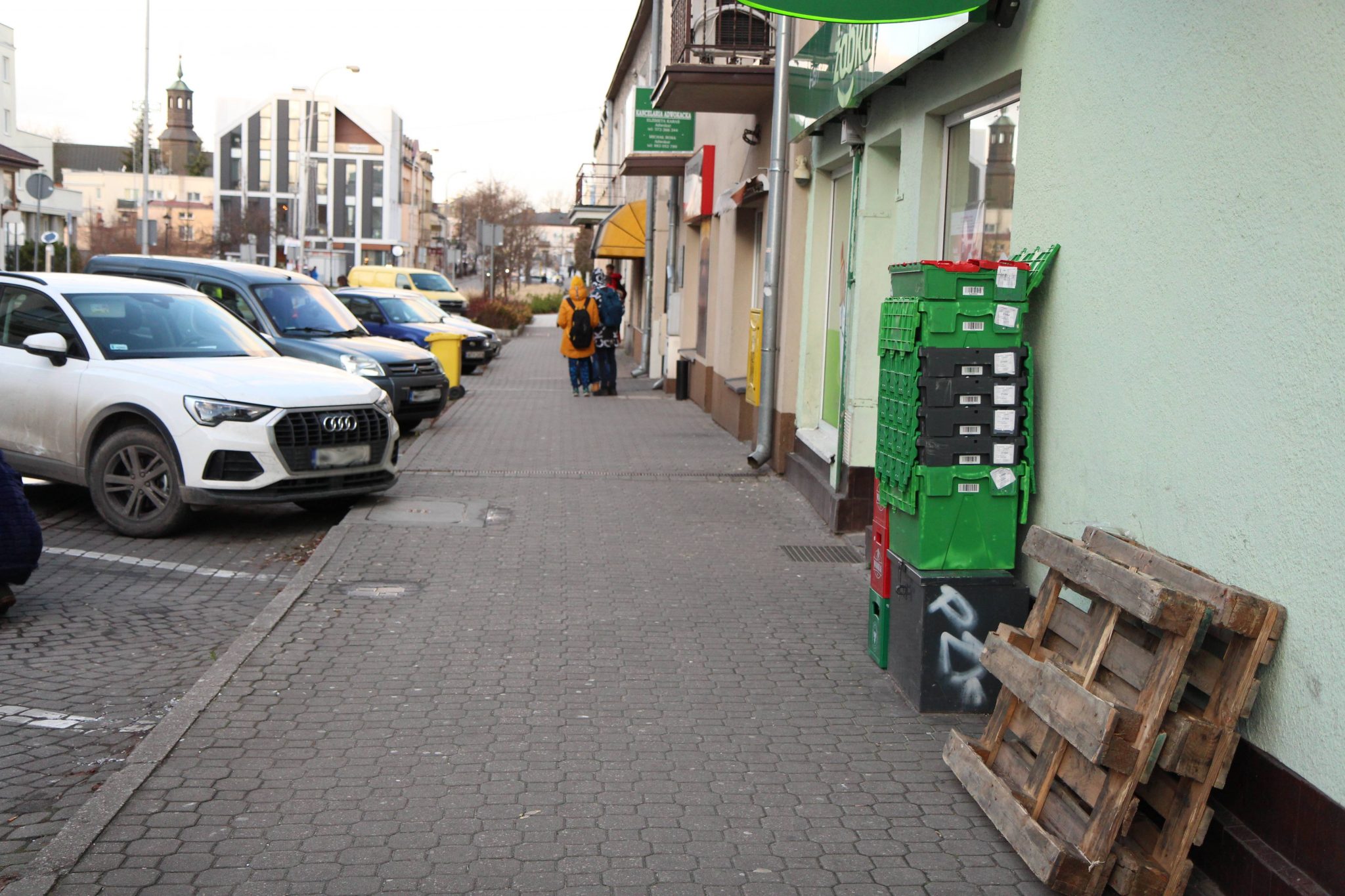 Patrzymy w przyszłość – zmieniamy centrum miasta. Na zdjęciu ulica Kościuszki, na chodniku wystawione transportery ze sklepu, przy chodniku zaparkowane samochody.