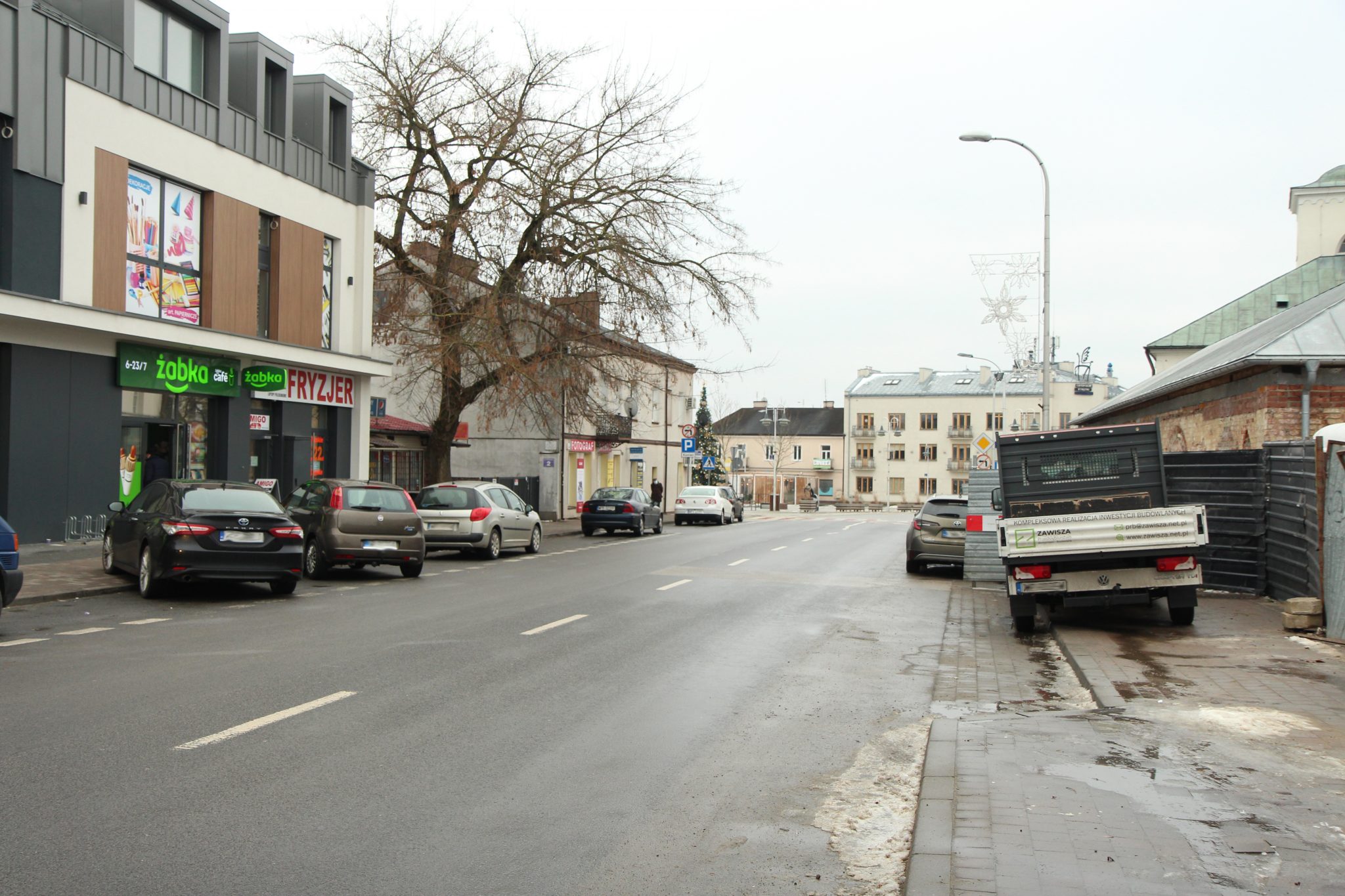 Gmina planuje przebudowę kolejnego odcinka głównej arterii miasta. na zdjęciu ulica Puławska z parkującymi po obu stronach samochodami.