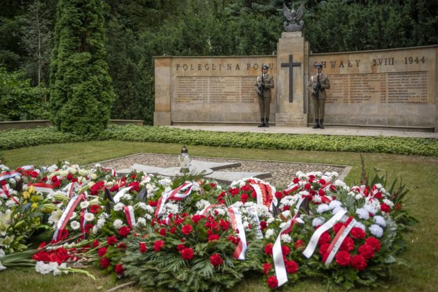 Pomnik Mauzoleum w Pęcicach. Przy pomniku dwaj żołnierze. Obok wieńce z biało-czerwonych kwiatów.,