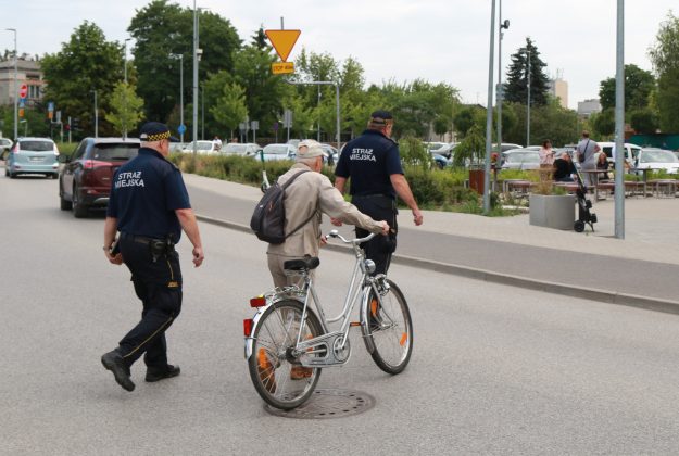 Rowerzyści łamiący przepisy będą karani. Na zdjęciu rowerzysta i dwóch strażników.