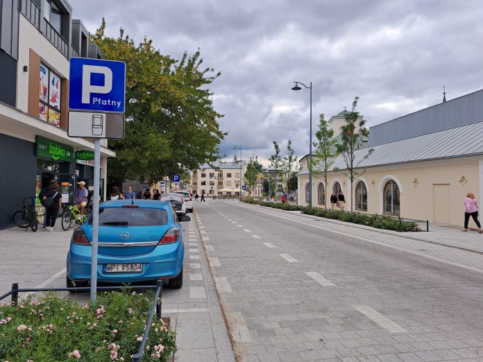 ulica Puławska, na zdjeciu budynki i niebieski samochód.