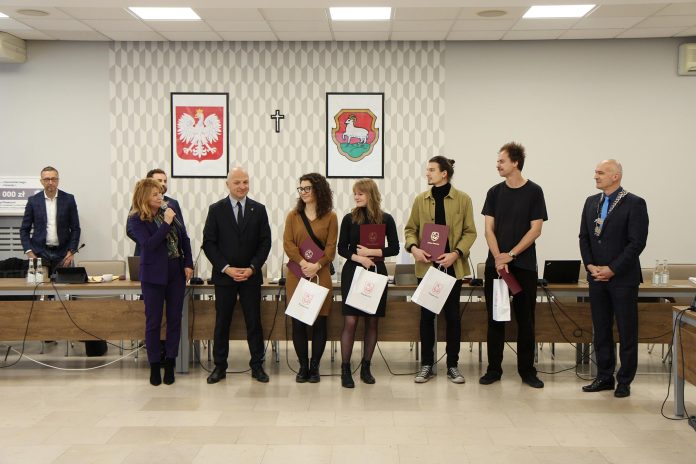 czworo stypendystów na sesji rady miejskiej, uhonorowani na środku sali.