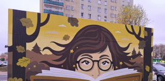 Mural Biblioteki. Namalowana twarz w okularach wystająca zza ksiązki, wokół liście dębu, kolorystyka jesienna.