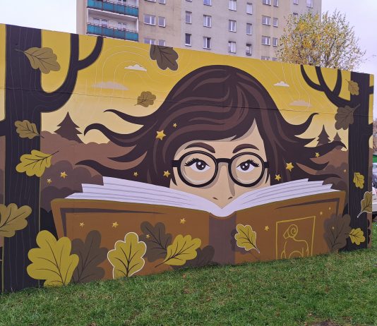 Mural Biblioteki. Namalowana twarz w okularach wystająca zza ksiązki, wokół liście dębu, kolorystyka jesienna.