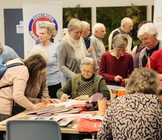 grupa seniorów przy stolikach konsultuje się z ekspertami