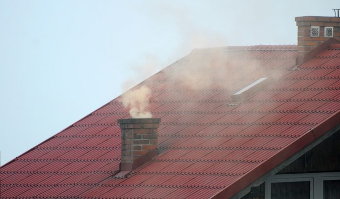komin na dachu z którego wydobywa się brudny dym