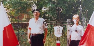Brunon Kreft. Na zdjęciu mężczyzna i chłopiec na cmentarzu, obok flagi narodowe.