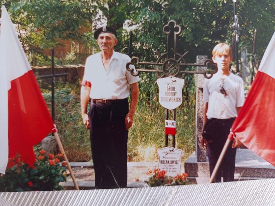Brunon Kreft. Na zdjęciu mężczyzna i chłopiec na cmentarzu, obok flagi narodowe.