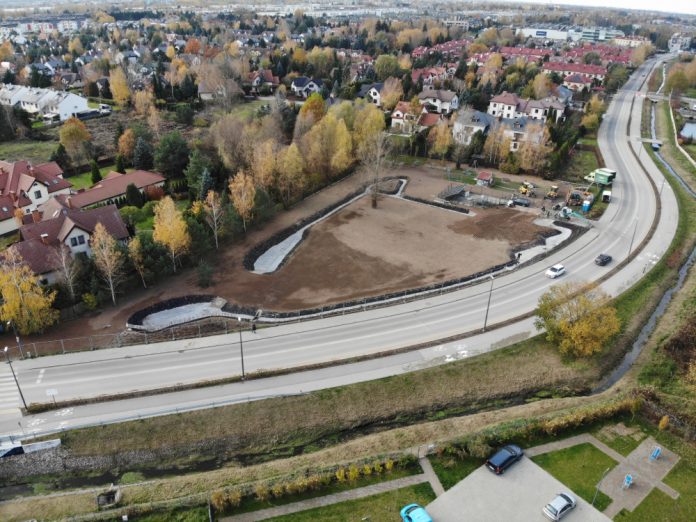 Błękitno-zielona infrastruktura przy ul. Cyraneczki . Na zdjęciu droga, domy, drzewa, budowany rów odwadniający.