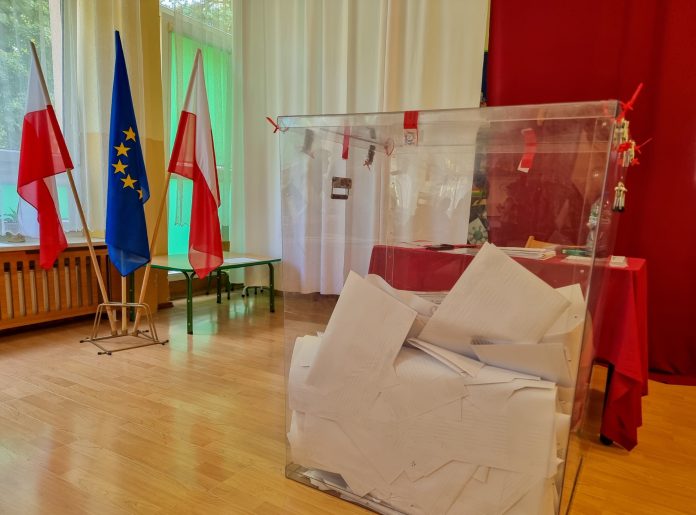 wybory PE. Na zdjęciu urna wyborcza, w tle flagi Polski i Unii Europejskiej