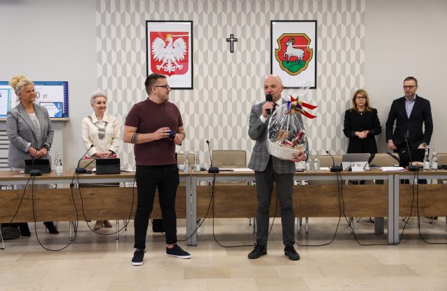 na zdjęciu kilka osób, burmistrz mówi do mikrofonu i trzyma kosz upominkowy