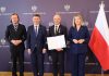 trzech mężczyzn i kobieta, obok polska flaga