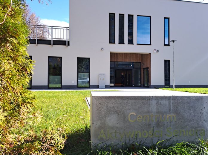 przystan pod klonami biały budynek, w pierwszym planie kamień z napisem: Centrum Aktywności Seniora