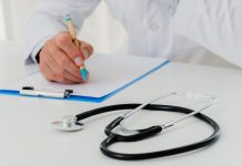 słuchawki lekarskie i dłoń z długopisem oparta o kartkę na biurku