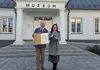 Burmistrz i dyrektor muzeum pozują pod budynkiem muzeum z dyplomem i medalem