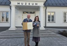 Burmistrz i dyrektor muzeum pozują pod budynkiem muzeum z dyplomem i medalem