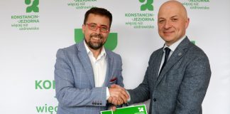 dwóch mężczyzn -uścisk ręki, w drugich dłoniach trzymają zielone teczki