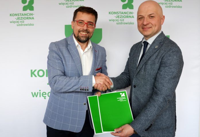 dwóch mężczyzn -uścisk ręki, w drugich dłoniach trzymają zielone teczki