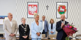 grupa osób, burmistrz trzyma bukiet i mówi do mikrofonu