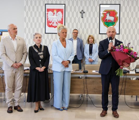 grupa osób, burmistrz trzyma bukiet i mówi do mikrofonu