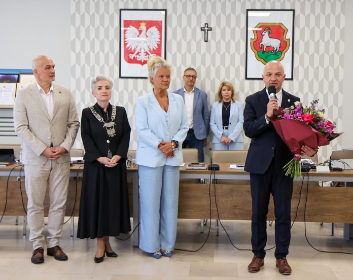 grupa osób, burmistrz trzyma bukiet i mówi do mikrofonu