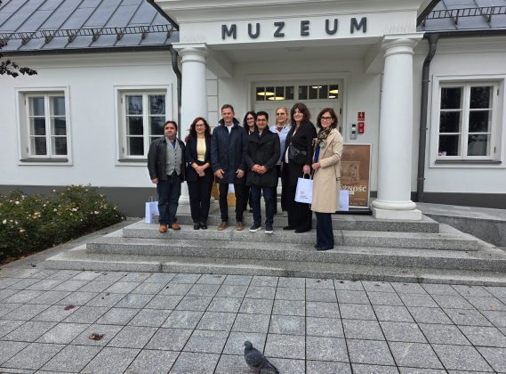 grupa os&oacute;b przed muzeum, na pierwszym planie gołąb